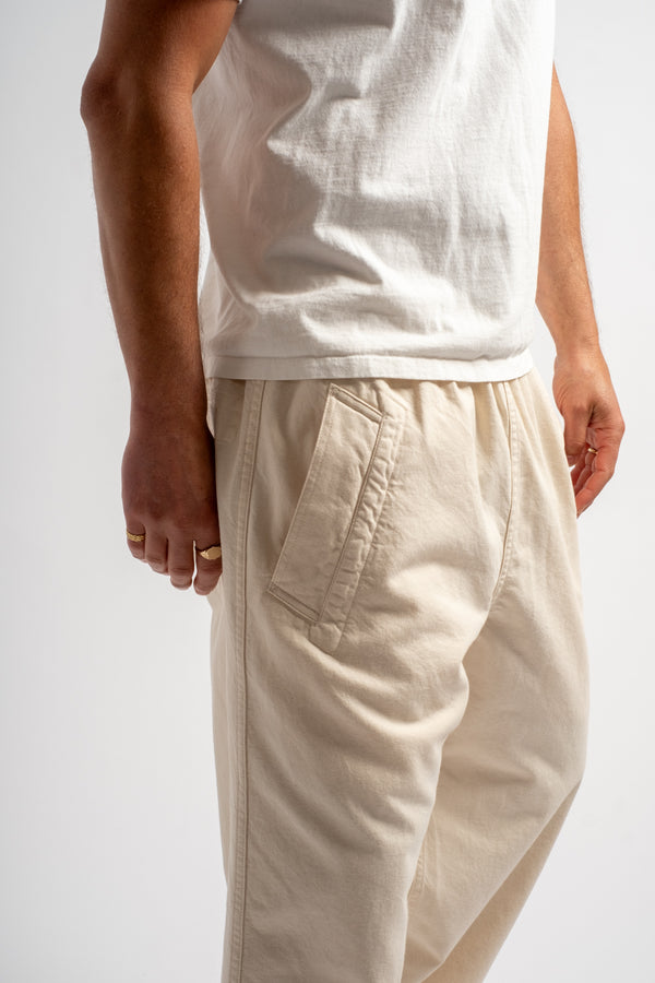 Person wearing a white sleeveless top and beige pants on a plain background