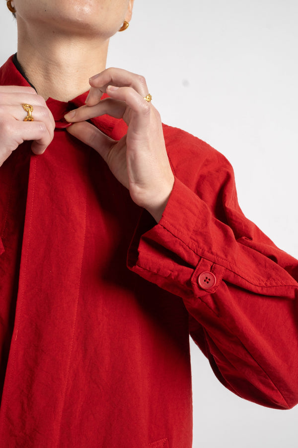 Person wearing a red shirt with rolled-up sleeves, adjusting the collar against a white background