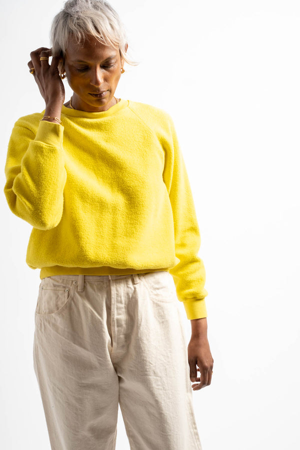 Person wearing a bright yellow sweater and light-colored pants on a white background