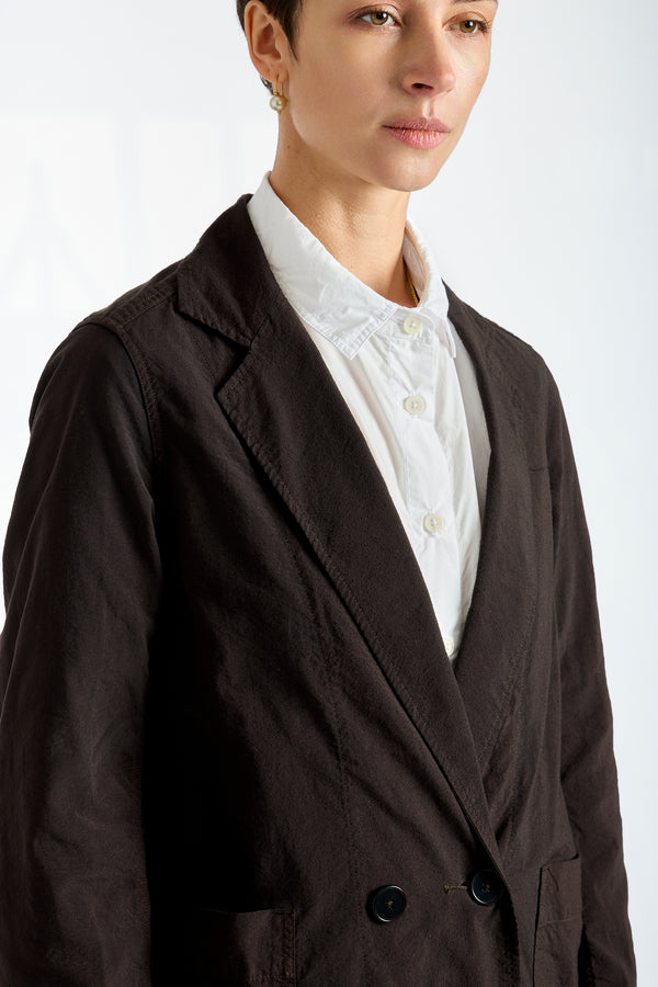Woman wearing a dark brown blazer over a white blouse on a plain background
