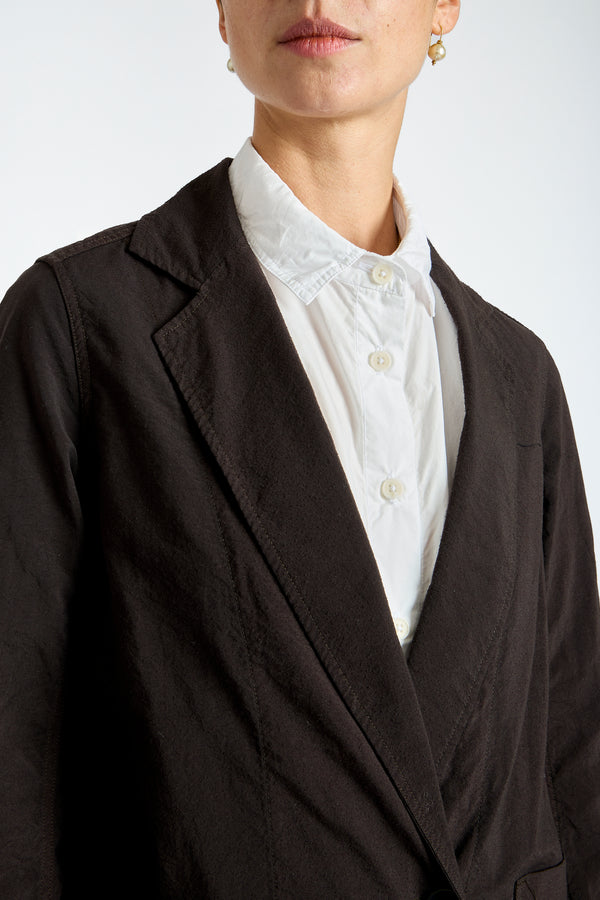 Person wearing a black blazer over a white shirt with lace details on a plain background