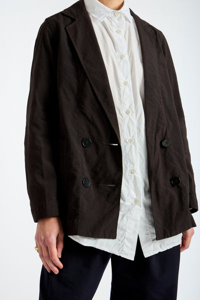 Person wearing a brown blazer over a white shirt with lace details on a white background