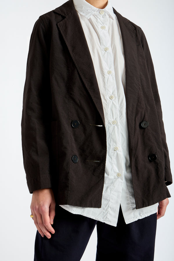 Person wearing a brown blazer over a white shirt with lace details on a white background